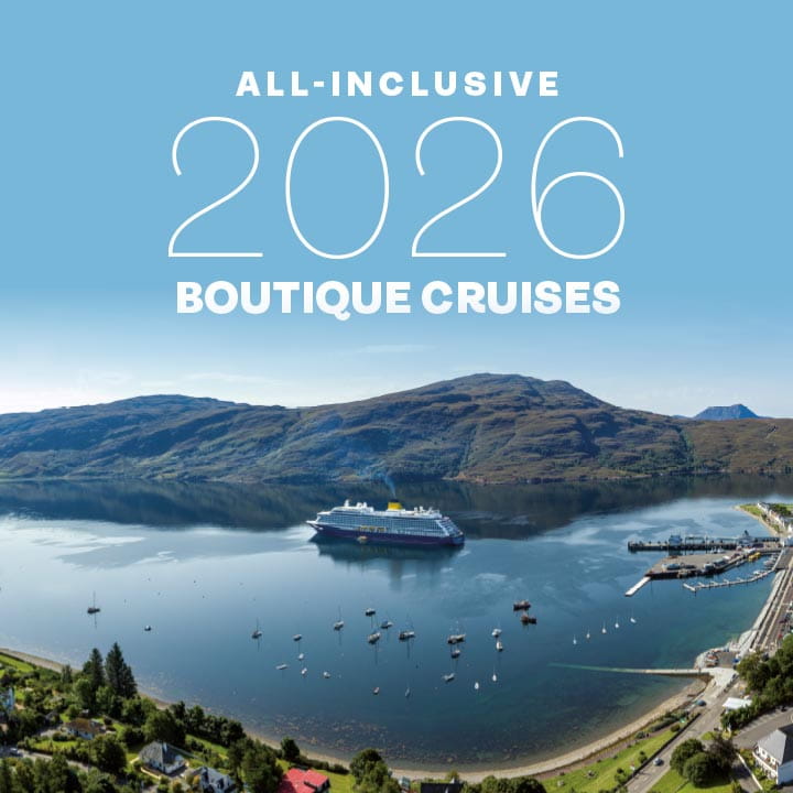 White text that reads 'All-inclusive 2026 boutique cruises' overlaid on an image of Spirit of Adventure in Ullapool, UK, on a sunny day. Image Credit © Steven Gourlay Media
